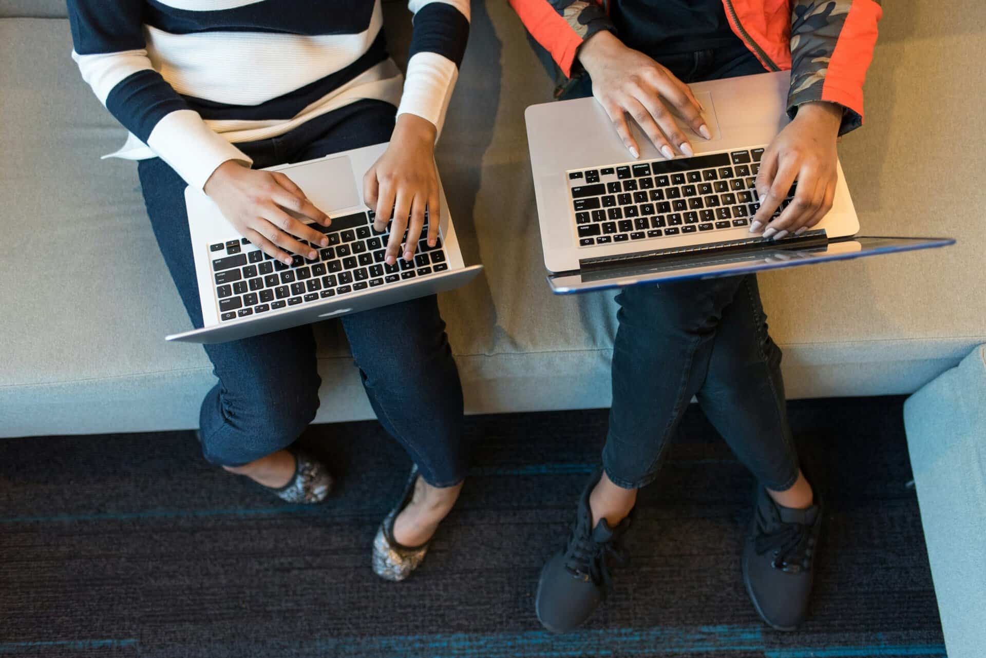 Two people sitting side by side working on laptops in a shared workspace.