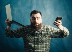 Person facing the screen holding a phone and a laptop