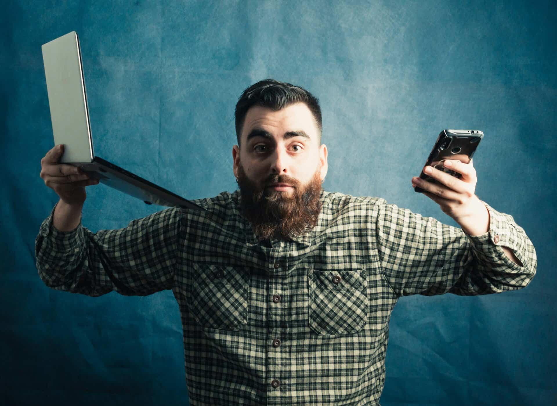 Person facing the screen holding a phone and a laptop